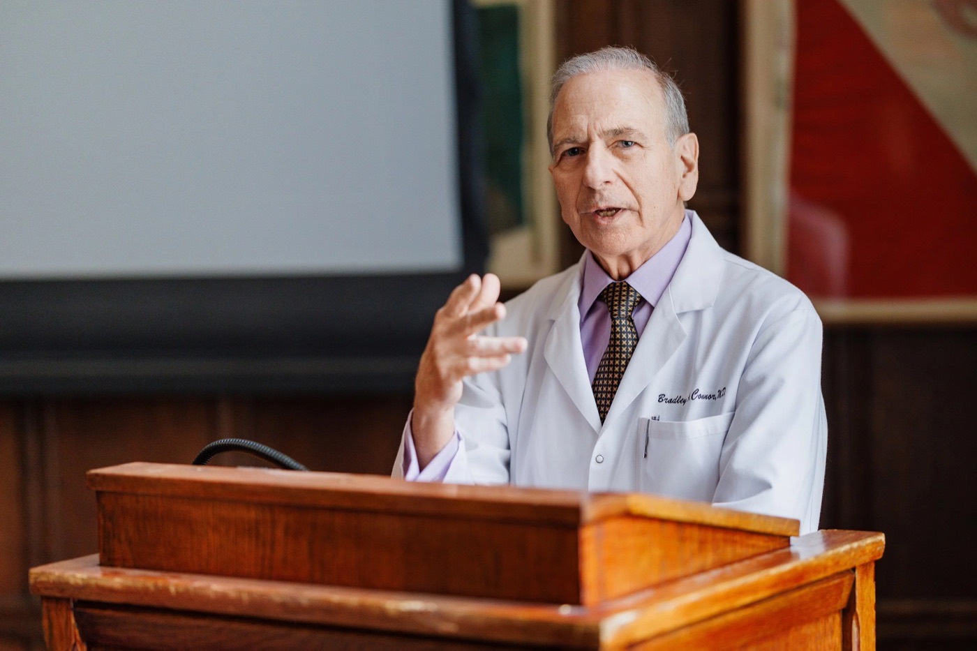 Dr. Bradley A. Connor in a white coat speaking from a wooden lectern