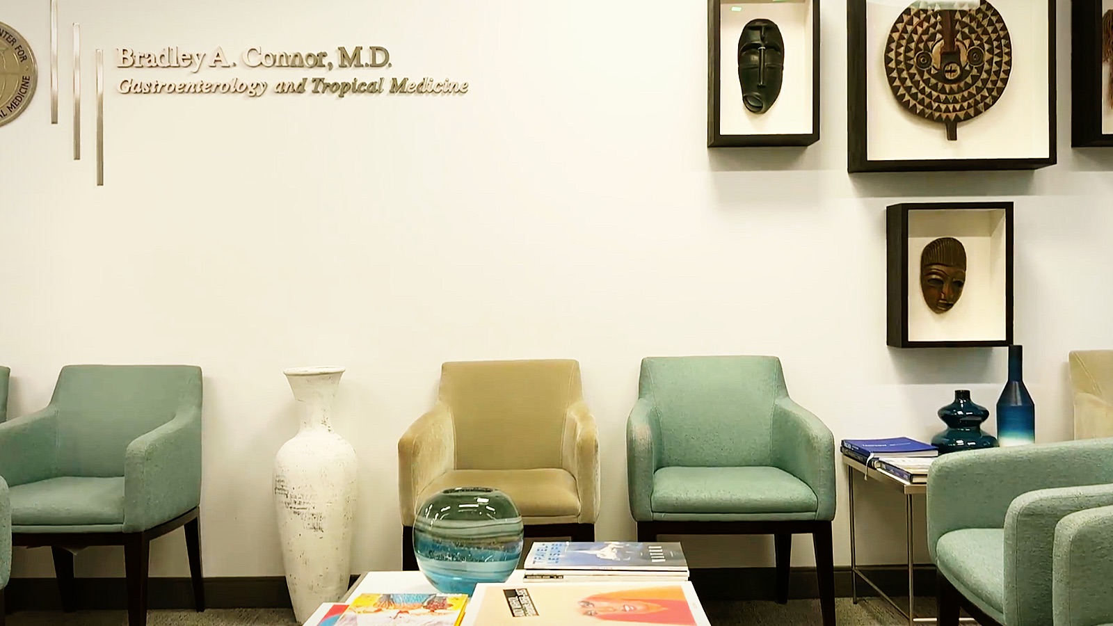 Waiting room with teal armchairs and framed masks on the wall