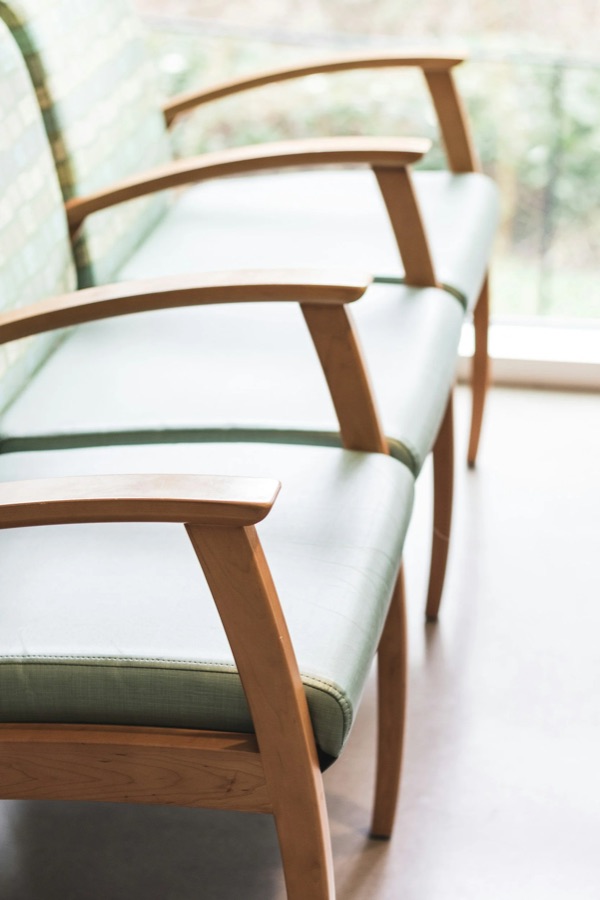 Wooden armchairs with pale green upholstery along a window in the clinic's waiting room